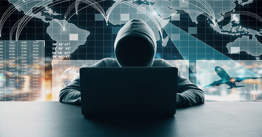 Dark Web danger represented by a hacker in a hoodie hunched over a black computer in front of a glowing world map representing records on the dark web