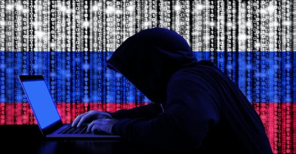 us government hack by suspected russsian cybercriminals represented by a hacker in a hoodie in silhouette against a russioan flag created in binary code
