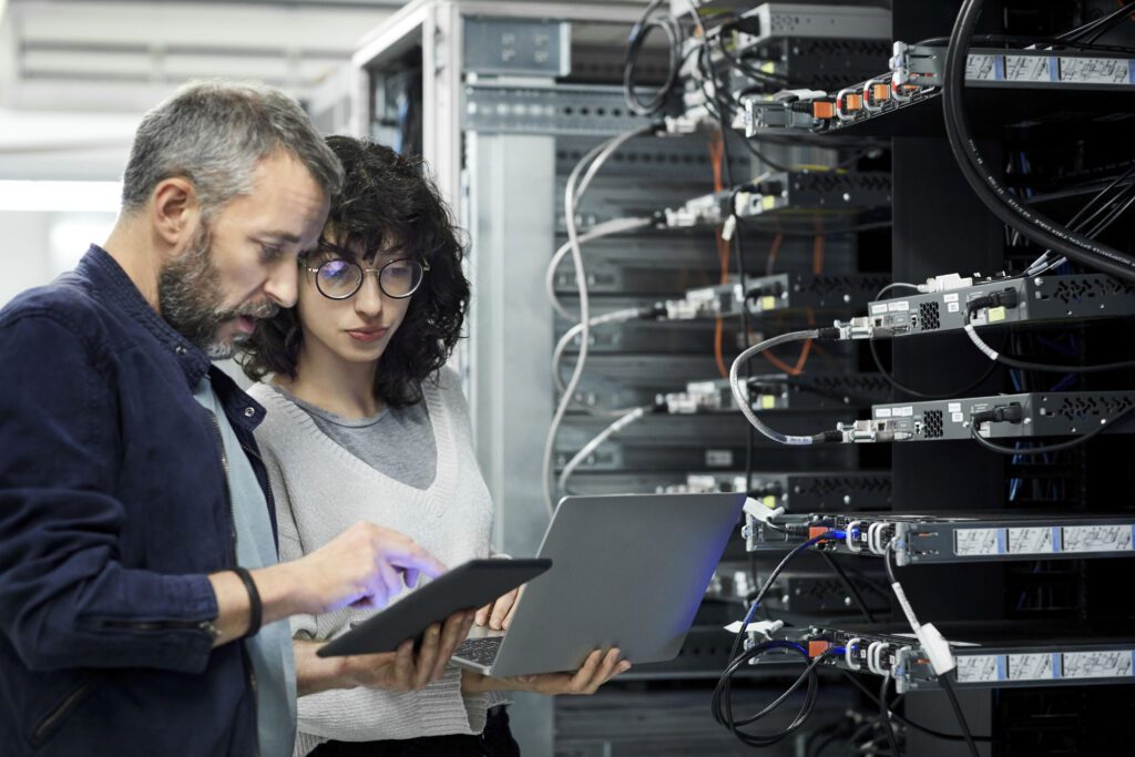 Bearded Male technician showing digital tablet to a white female coworker in server room.