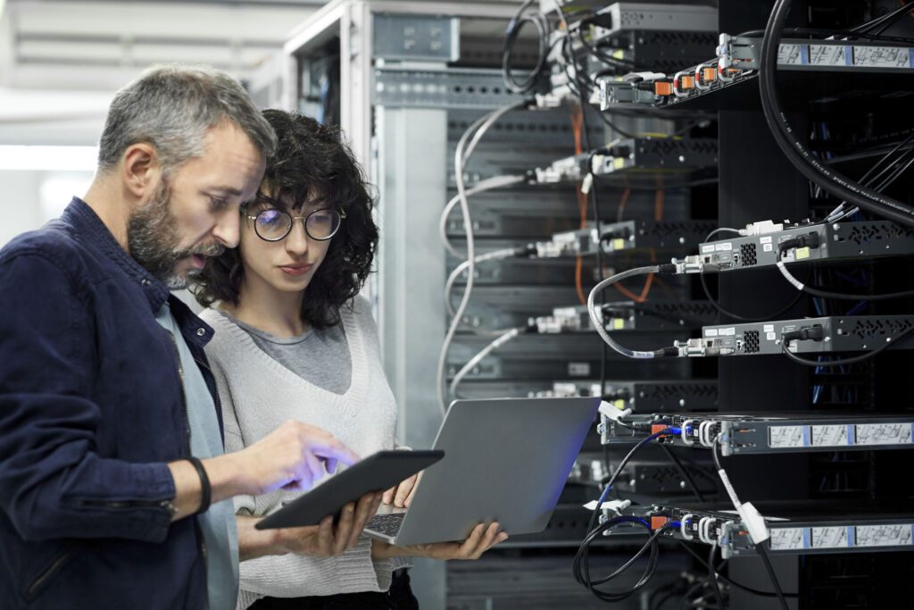 managed SOc represented byBearded Male technician showing digital tablet to a white female coworker in server room.