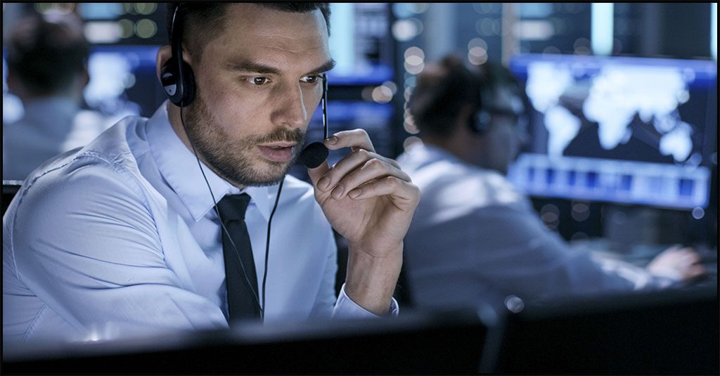 managed SOc represented by a white man at a computer talking on a headset surrounded by other screens of data